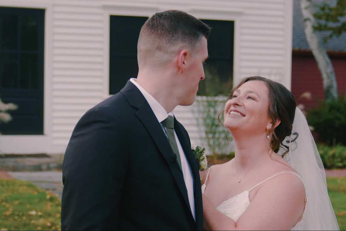 Groom dipping the bride for a kiss on a hillside lawn beside a white gazebo, her veil trailing in the wind