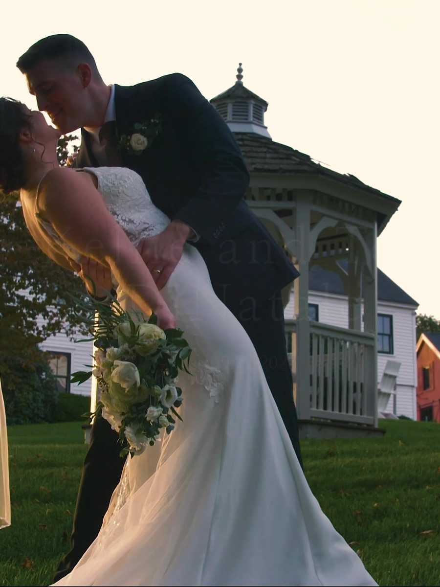 Bride laughing up at the groom in front of a white New England farmhouse, veil draped over her shoulder